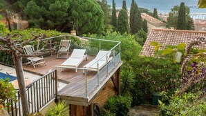 Une terrasse avec des chaises longues donnant sur un jardin et offrant une vue sur la côte.