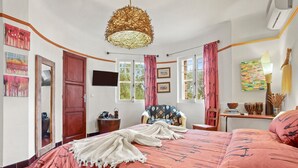 Une chambre avec un grand lit, une porte en bois, une télévision et des œuvres d’art accrochées aux murs.