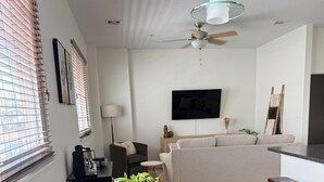 Un salon moderne avec une table en bois foncé, deux fauteuils beige, une plante en pot et un canapé gris.