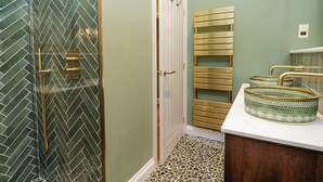 A bathroom with a herringbone tile shower, a white door, a gold towel rack, and a green patterned sink. - The Studio (Windermere)