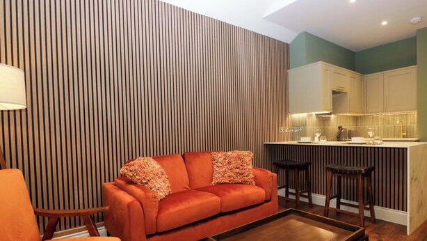 A modern living room with a sofa, a coffee table, and a kitchen area with bar stools. - The Studio (Windermere)