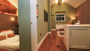 A hotel room with a bed, a small kitchenette, a window, and a door leading to another room. - The Studio (Windermere)