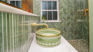 A bathroom with a green and white herringbone tile pattern, a gold faucet, and a green patterned basin. - The Studio (Windermere)