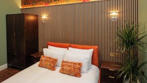 A bedroom with a bed, two pillows, a nightstand, a wardrobe, a wall with vertical wooden slats, and a decorative panel with floral designs. - The Studio (Windermere)