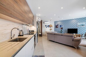 Een moderne keuken met een spoelbak, fornuis en magnetron, een woonruimte met een bank en televisie, en een muur met een wereldkaart en kunstwerken.