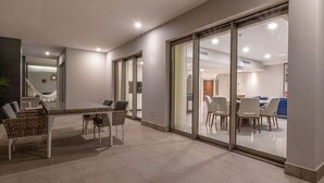 A modern interior with a dining area featuring a glass table and chairs, a visible kitchen area, and a large sliding glass door leading to another room. - 4,198-square-foot oceanfront suite is chic and modern (Aurora)