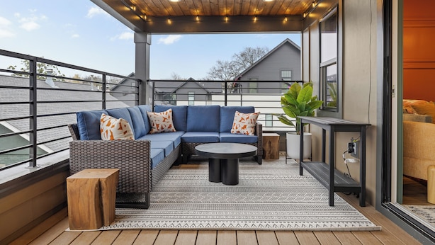 Een terras buiten met een blauwe bank, een ronde tafel en houten krukken.