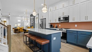 Een moderne keuken met een centraal eiland, barstoelen, witte kasten en roestvrijstalen apparatuur.