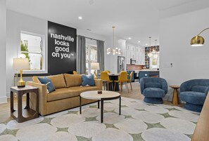 Ein modernes Wohnzimmer mit Sofa, Sesseln, einem Couchtisch und einer Küche im Hintergrund.