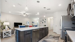 A modern kitchen with a central island, stainless steel appliances, pendant lighting, and a ceiling fan. - Serenity by the Sea - For 6 (St. Augustine)