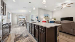 A modern kitchen with dark cabinets, a large island, pendant lights, and a ceiling fan. - Serenity by the Sea - For 6 (St. Augustine)