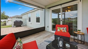 A covered patio with a glass door leading to a backyard, a red sofa, a small table, and a grill. - Serenity by the Sea - For 6 (St. Augustine)