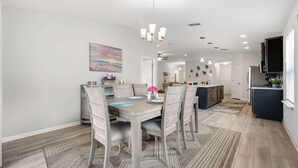 A modern kitchen with a central island, pendant lighting, and a dining area with a table set for four. - Serenity by the Sea - For 6 (St. Augustine)