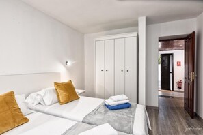 Ein Hotelzimmer mit zwei Betten, einem Kleiderschrank, einem Nachttisch und einem Flur, der zu einem Ausgang führt.