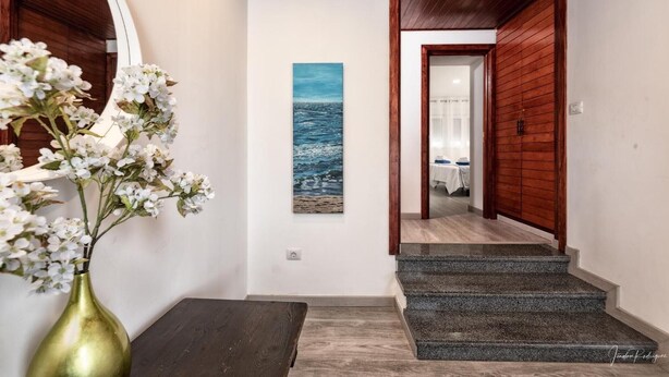En hall med ett träpanelat tak, en målning som föreställer havet, en vas med blommor och en trappa.