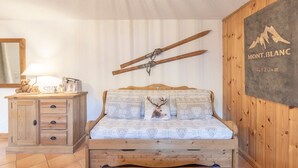 Una cama de madera con ropa de cama estampada, un aparador de madera, una lámpara y un esquí de pared.