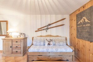 A wooden bed with patterned bedding, a wooden dresser, a lamp, and a wall-mounted ski rack. - Cosy Apartment in Central Samoëns with Mountain View, Balcony, Near the Slopes (Samoëns)
