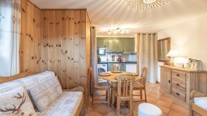 Una habitación acogedora con un muro de madera, una mesa de comedor con sillas, un sofá y una cocina al fondo.