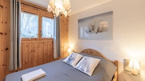 Una habitación con una cama, paredes de madera, una ventana con cortinas, una lámpara de pared y un cuadro enmarcado.