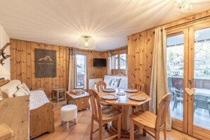 A wooden interior with a dining table, chairs, a sofa, and a television. - Cosy Apartment in Central Samoëns with Mountain View, Balcony, Near the Slopes (Samoëns)