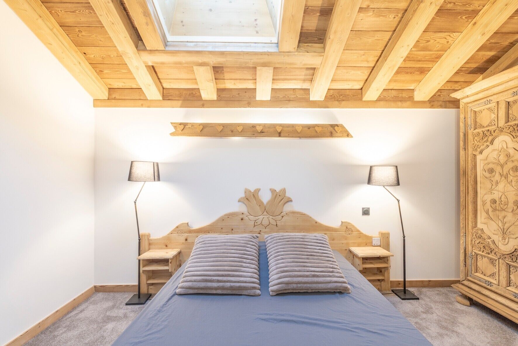 A bedroom with a wooden headboard, two bedside lamps, a skylight, and a carpeted floor.