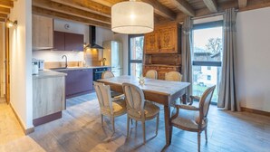 A modern kitchen with wooden cabinets, a dining table with chairs, and a large window. - Apartment 'Morillon – New – 2 min from the slopes' with mountain view, private terrace (Morillon)