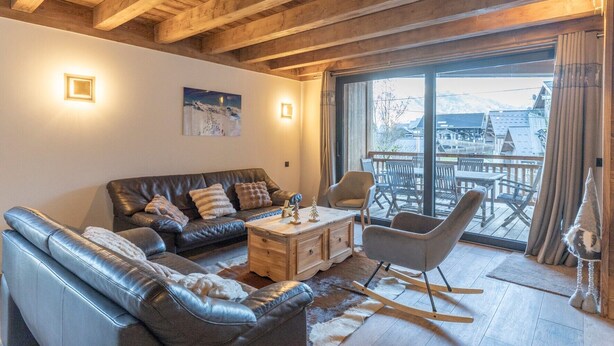 A cozy living room with a leather sofa, a wooden coffee table, and a rocking chair. A large window offers a view of the outside. - Apartment 'Morillon – New – 2 min from the slopes' with mountain view, private terrace (Morillon)