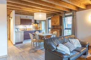 Una cocina moderna con armarios de madera, un comedor con mesa y sillas, y un sofá de cuero con un cojín decorativo.