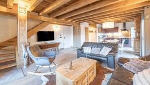 A spacious loft with exposed wooden beams, a living area with a sofa and armchairs, a dining area with a table and chairs, and a kitchen with modern appliances. - Apartment 'Morillon – New – 2 min from the slopes' with mountain view, private terrace (Morillon)