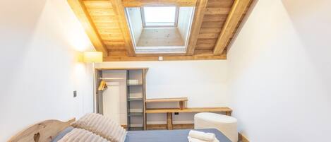 A bedroom with a skylight, a bed with pillows, a bedside table, a bench, and a wardrobe.