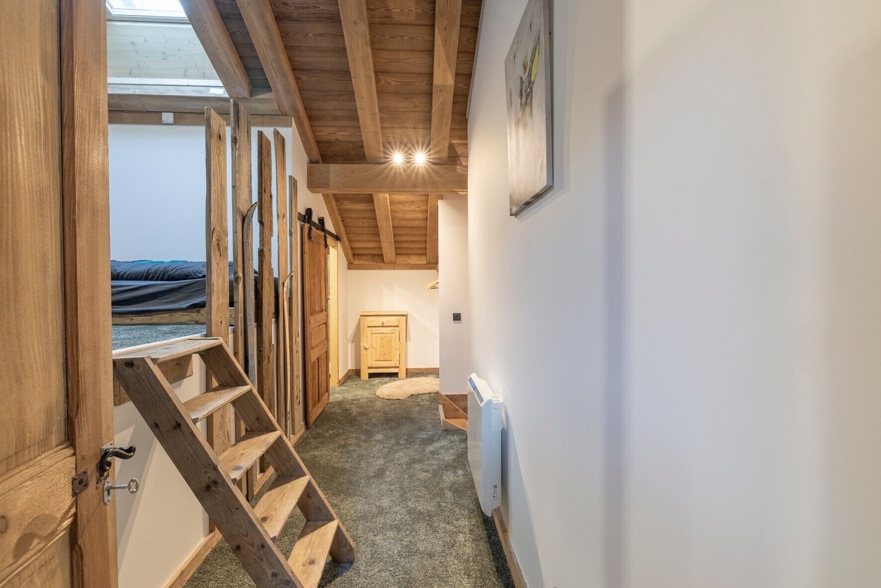Una escalera de madera que conduce a un dormitorio en un altillo con un tragaluz, un radiador y un cuadro en la pared.