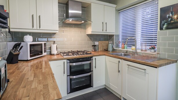 Een moderne keuken met witte kastjes, een ingebouwde magnetron, een gasfornuis en een oven.