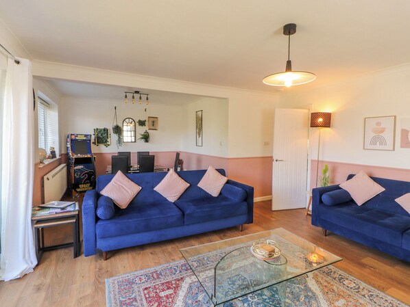 A living room with two blue sofas, a glass coffee table, and a space-themed arcade game. - Lake View (Windermere)