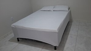 A single bed with a white mattress and pillows, a curved footboard, and black legs. The room has white walls and a tiled floor. - Esmeraldas Garden Site, a peaceful place with a wonderful view and a swimming pool. (Esmeraldas)