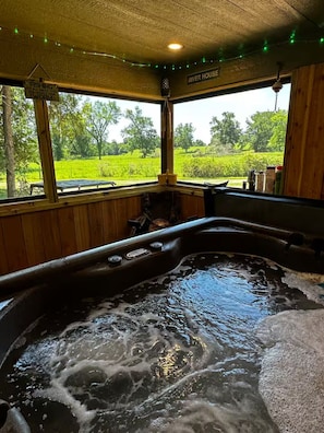 Ett bubbelbad med utsikt över ett grönskande landskap genom stora fönster.
