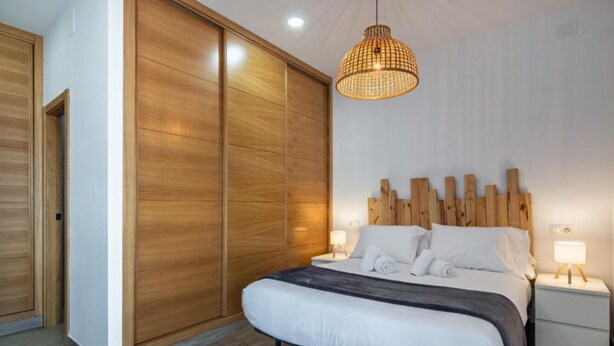 Un dormitorio con cama, armario de madera, lámparas de noche y una lámpara colgante.