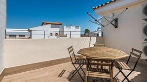 Terraza en la azotea con una mesa y sillas de madera, un tendedero y vistas a edificios al fondo.