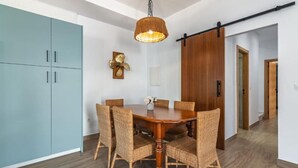 Un comedor con una mesa de madera y sillas de mimbre, una l ámpara colgante y una puerta corredera.