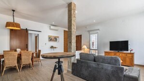 Una sala de estar con sofá, una mesa de comedor con sillas, un televisor y un pilar de piedra.