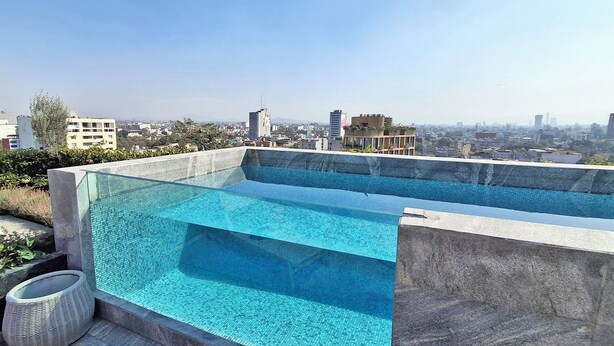 A rooftop infinity pool with a city view, surrounded by stone walls and a wicker chair. - Luxury loft Roma Norte with pool, gym, AC & cowork (Ciudad de México)