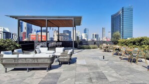 An outdoor seating area with wicker furniture and a covered seating area, overlooking a city skyline with modern buildings. - Luxury loft Roma Norte with pool, gym, AC & cowork (Ciudad de México)
