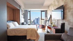 A modern hotel room with a large bed, a desk, a chair, a TV, and a view of the cityscape. - Luxury loft Roma Norte with pool, gym, AC & cowork (Ciudad de México)