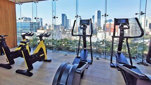 A gym with exercise equipment and a city view through large windows. - Luxury loft Roma Norte with pool, gym, AC & cowork (Ciudad de México)