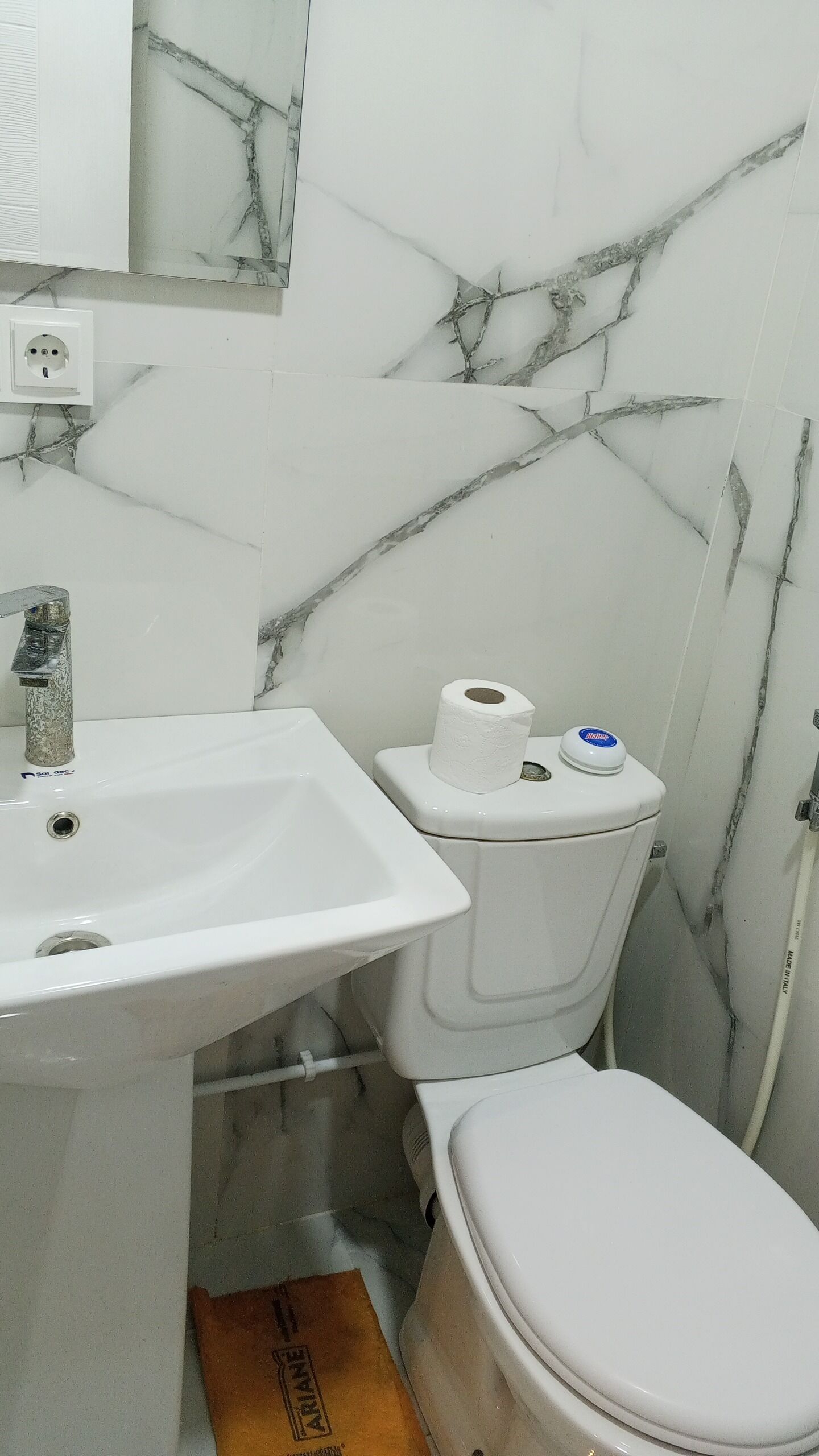 Un baño con lavamanos blanco, inodoro y paredes con diseño de mármol.