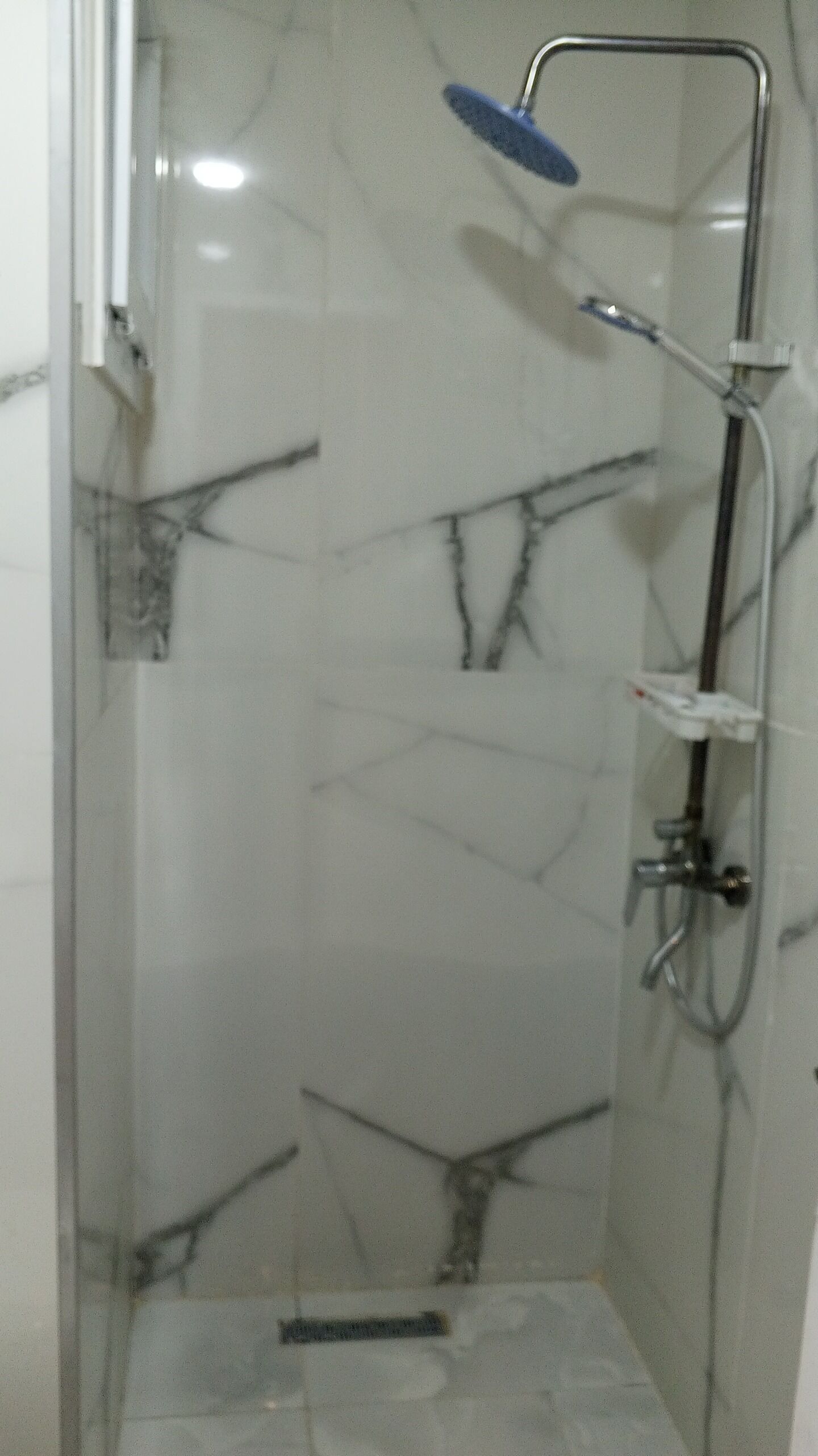 A bathroom with a glass shower enclosure, a white marble wall, and a handheld showerhead.