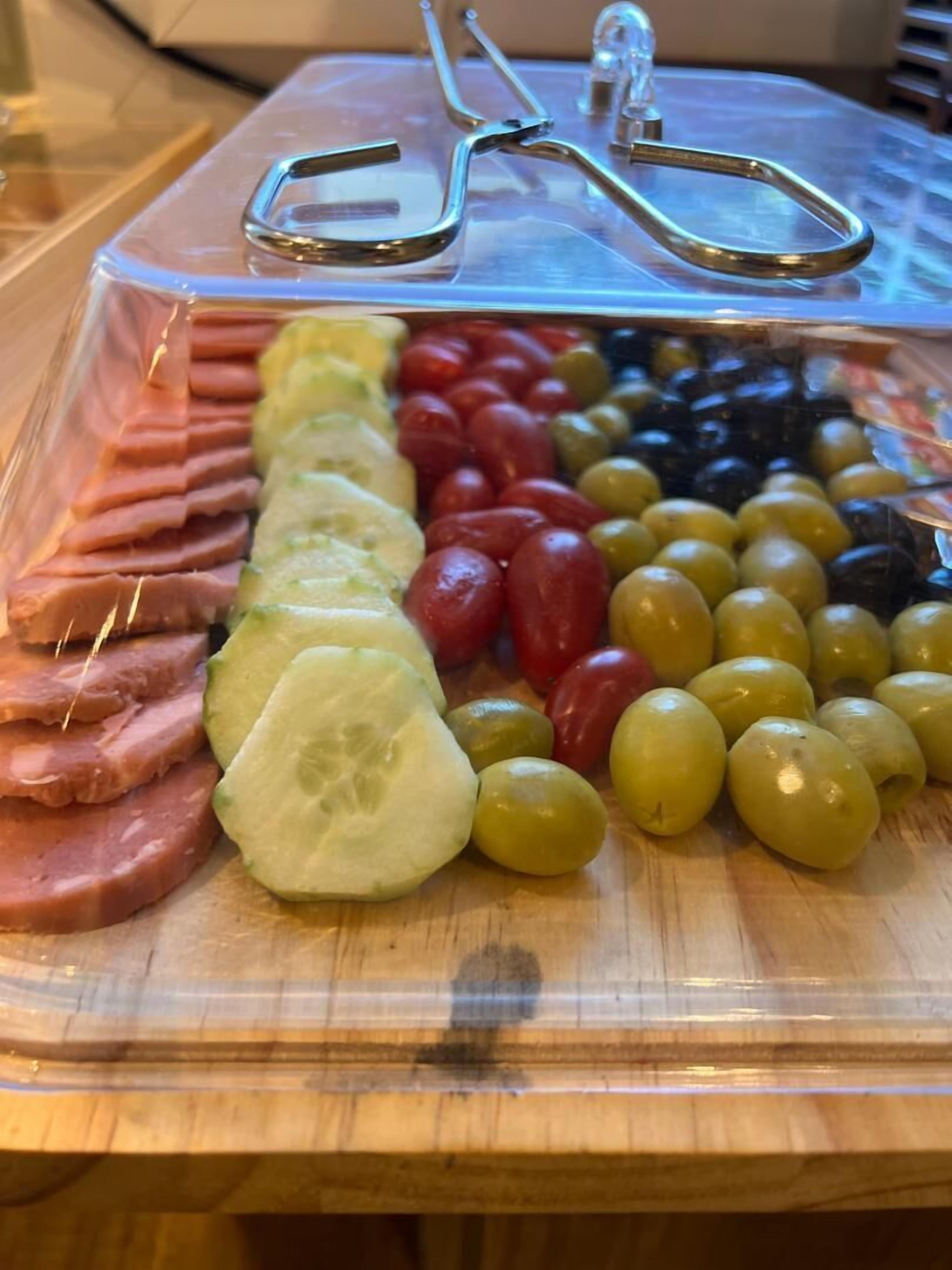 A charcuterie board with sliced ham, cucumbers, cherry tomatoes, and olives.