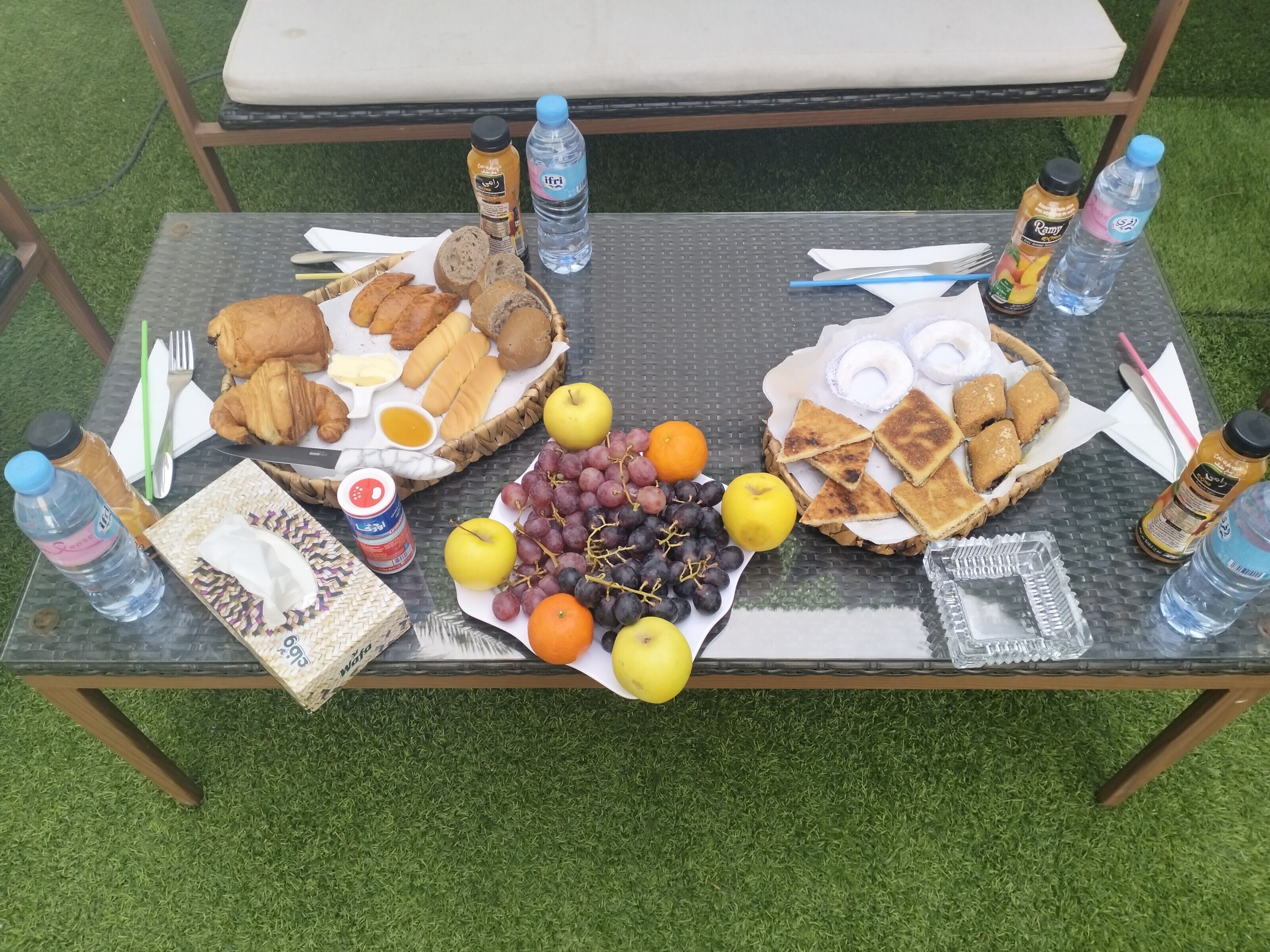 Una mesa al aire libre con alimentos, incluyendo pan, frutas y salsas.