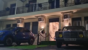 Un edificio con dos coches aparcados, una barrera de cuerda roja y un balcón con barandillas negras.