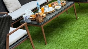 Un comedor con dos sillas de mimbre, una mesa de vidrio y una bandeja de desayuno con cruasanes, huevos y jugo de naranja.