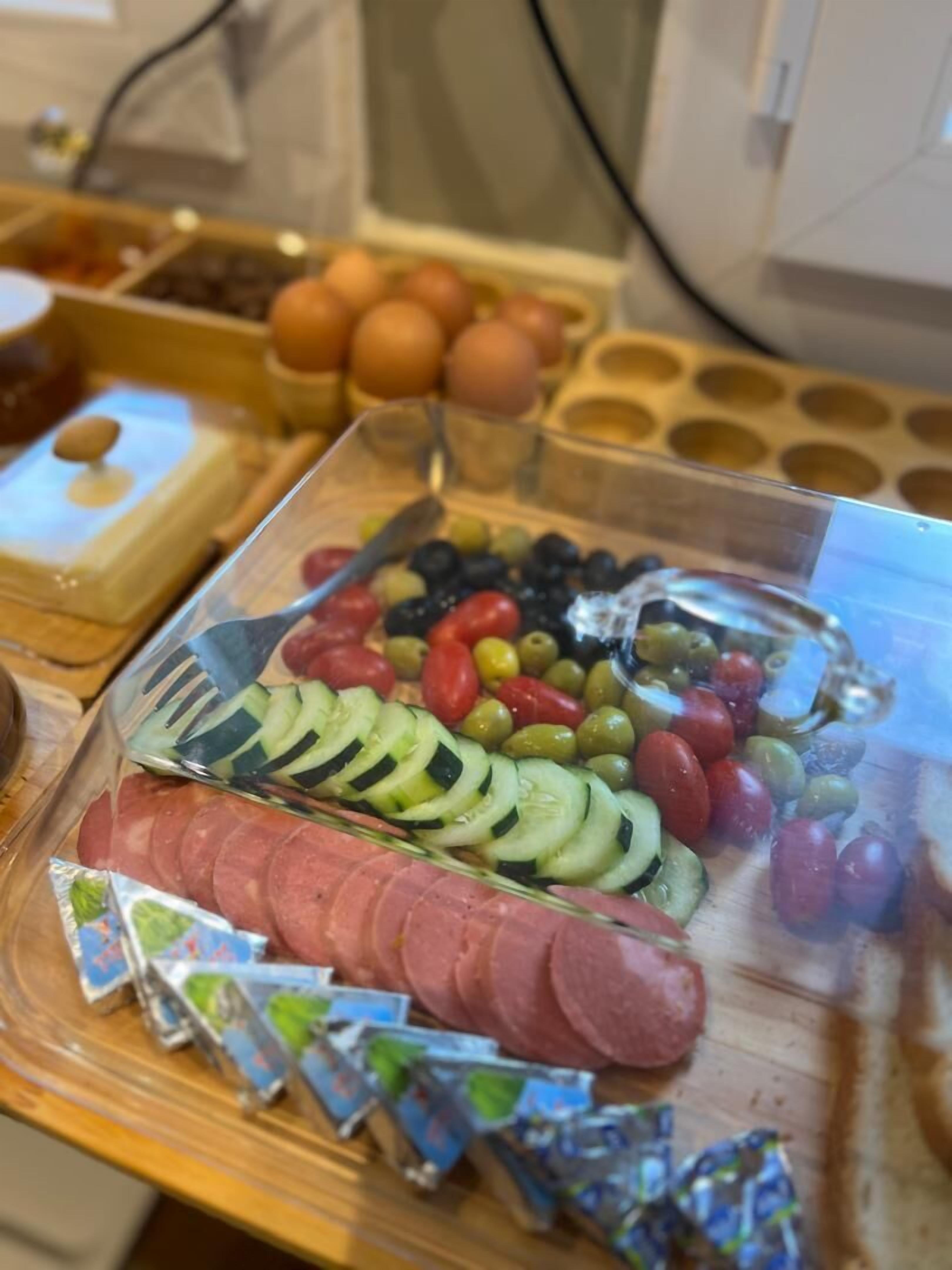 A buffet with sliced cucumbers, olives, tomatoes, and sausages.